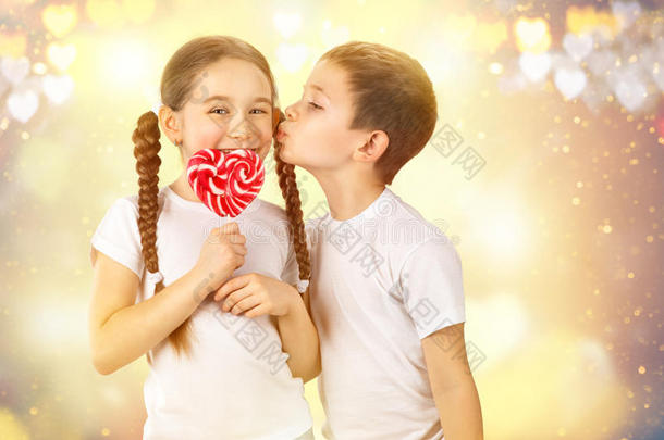 男孩用心形的糖果红色棒棒糖亲吻小女孩。 情人节`艺术肖像