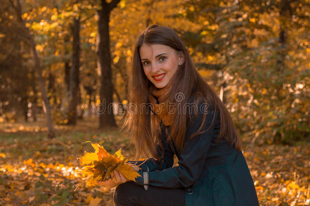 美丽的女孩留着长发和红色的口红，坐在公园里的树叶微笑