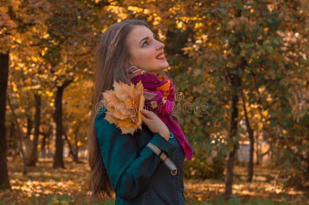 穿着粉红色围巾的可爱女孩站在公园里，把叶子放在手里