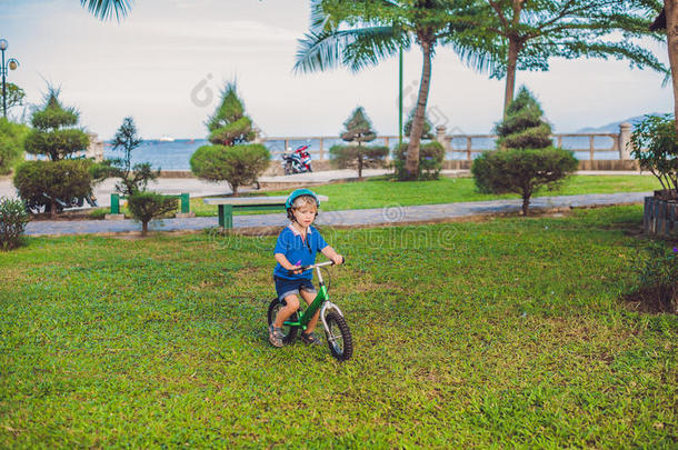 活跃的金发男孩在海边的公园里骑自行车。 蹒跚学步的孩子在温暖的夏天做梦和玩得开心。 在户外