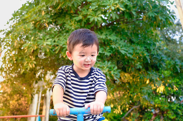 亚洲小孩在阳光下在操场上骑跷跷板，