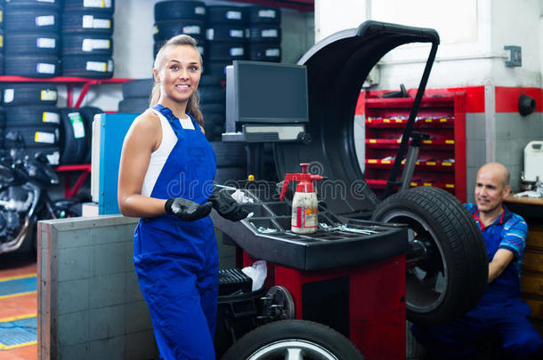 女技术员站在汽车车间与车轮平衡机械