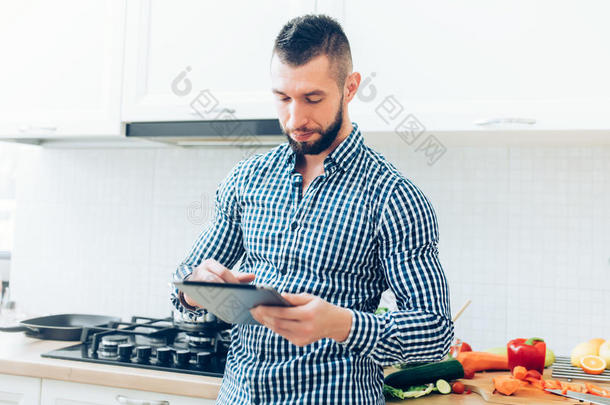 英俊的男人在厨房工作，仰望互联网收据。 现代厨师与平板电脑合作的细节
