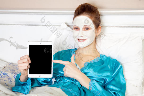 美丽的女人，绿色睡衣和白色面膜，躺在床上，在睡觉前拿着药片。