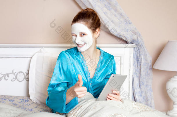 美丽的女人，绿色睡衣和白色面膜，躺在床上，在睡觉前拿着药片。