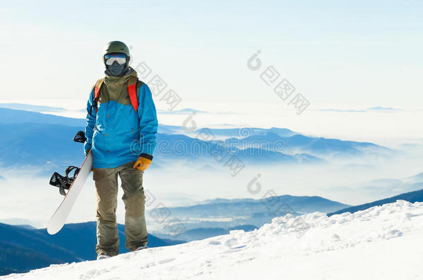 近距离拍摄年轻的滑雪者戴着头盔站在山顶，手里拿着他的滑雪板