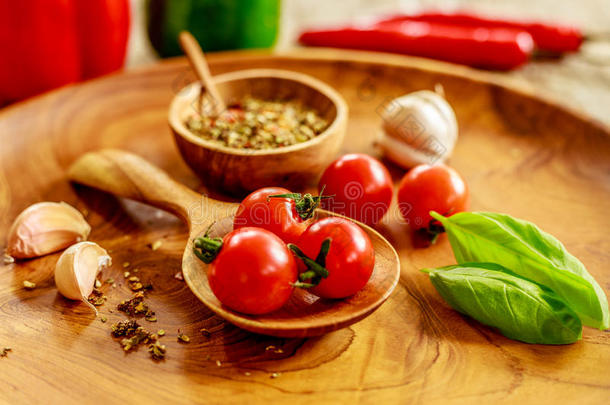 新鲜樱桃西红柿，大蒜，罗勒叶，混合干香料在木锅与木勺在木托盘上木桌，