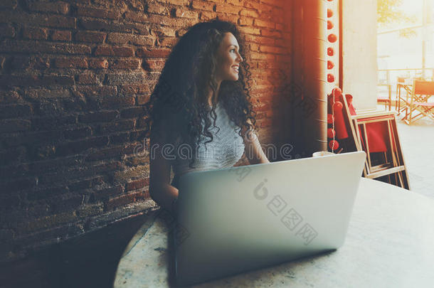 卷曲微笑的美丽女孩在咖啡馆的笔记本电脑上闲逛