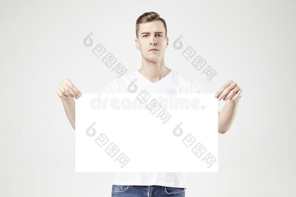 英俊的男人模型站在空白的大<strong>海报</strong>或床单在手，孤立在白色背景上，穿着<strong>牛仔</strong>裤和t恤。