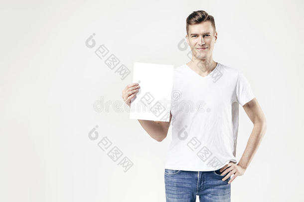 帅哥手里拿着<strong>白纸</strong>，孤立地站在白色背景上，穿着牛仔裤和t恤。 可用的文本空间