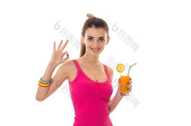 可爱的年轻黑发女孩，穿着浅色的夏季衣服，手里拿着橙色的鸡尾酒，在镜头上露出OK和微笑