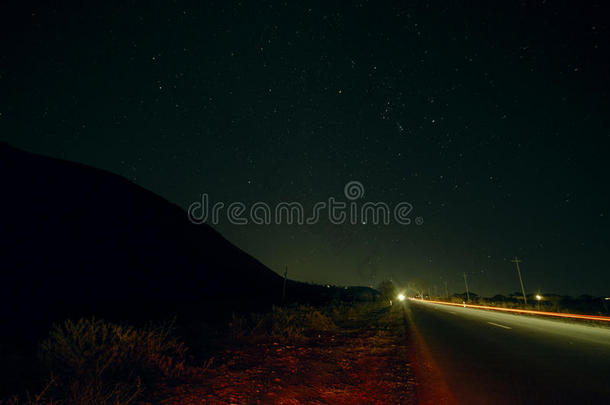 美丽的夜景，星星在天空和山脉轮廓附近的道路与汽车小径。 山中的道路在繁星下