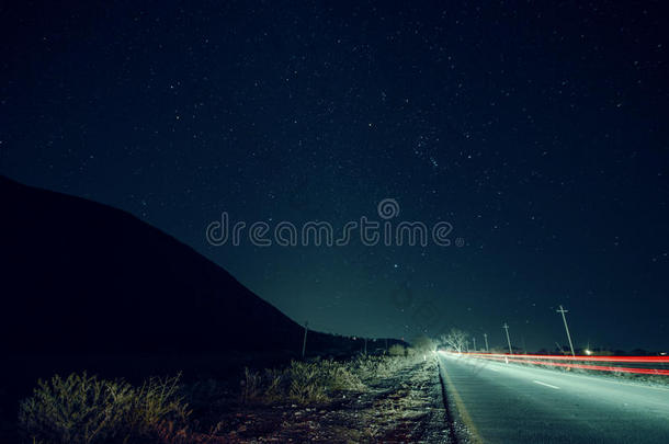 美丽的<strong>夜景</strong>，<strong>星星</strong>在天空和山脉轮廓附近的道路与汽车小径。 山中的道路在繁星下