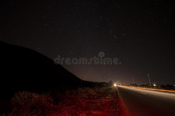 美丽的夜景，星星在天空和山脉轮廓附近的道路与汽车小径。 山中的道路在繁星下