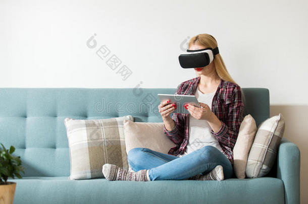 迷人的女人戴着虚拟现实眼镜躺在沙发上。 虚拟现实耳机。 生活方式虚拟现实概念。