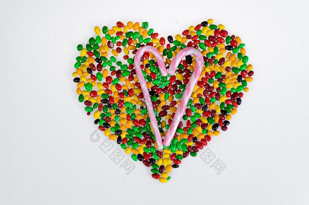 彩色果冻豆分散在心脏的形状和甜蜜的粉红色和白色条纹甘蔗在白色的背景。
