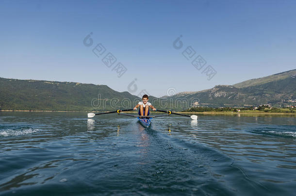 一位年轻的单人划艇<strong>选手</strong>在宁静的湖面上划桨