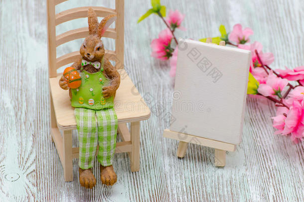 复活节兔子坐在凳子上，拿着一个鸡蛋，在木制背景上画画画架和花