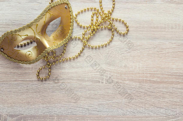 金色狂欢节面具和珠子在木制背景上。