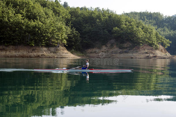 一位年轻的单人划艇选手在宁静的湖面上划桨