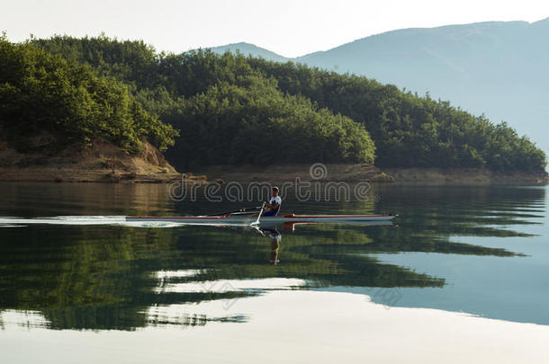 一位年轻的单人划艇选手在宁静的湖面上划桨