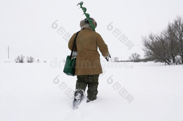 一个渔夫走在一个白雪覆盖的湖上，寻找一个好的钓鱼场所。