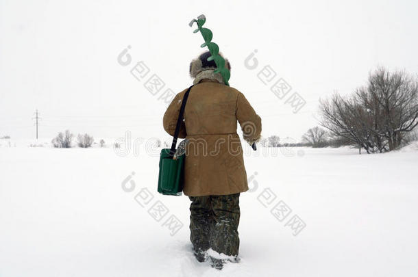一个渔夫走在一个白雪覆盖的湖上，寻找一个好的钓鱼场所。