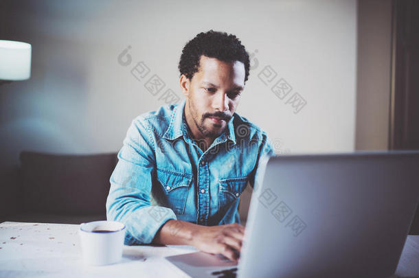 在木桌上的<strong>合作</strong>工作室使用笔记本电脑的忧郁胡须非洲男子的特写<strong>照片</strong>。年轻人的概念