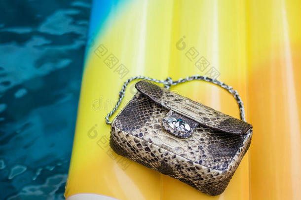 时尚豪华蛇皮蟒手提包在一个充气黄色床垫在游泳池。 夏天的心情。