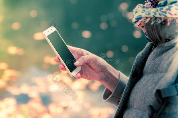 一张高角度的照片，一位黑发女人在公园散步，同时使用智能手机，湖在背景。