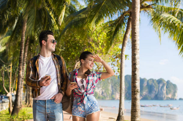 一对夫妇步行热带海滩棕榈树暑假，美丽的年轻人看着大海，男人女人度假