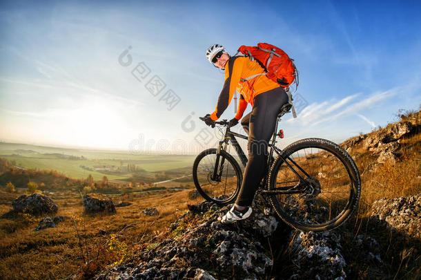 骑山地自行车的骑自行车者戴着头盔和眼镜，站在蓝天和阳光下的山崖上。 广角视图