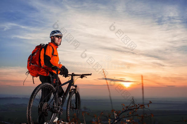 骑自行车的人靠在自行车上，在风景优美的天际线前观看日落。