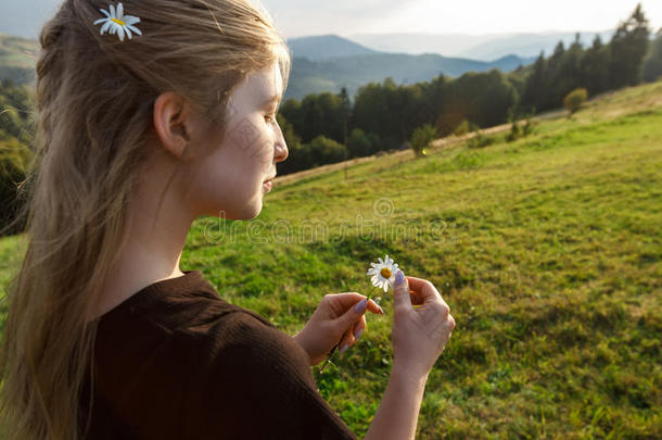 美丽的金发女孩抱着迷彩菊，卡帕西亚山脉的背景。