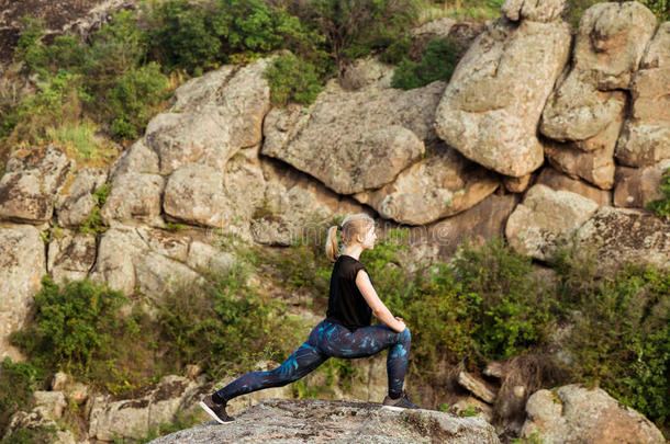 美丽的金发女孩训练，伸展在峡谷的岩石上。