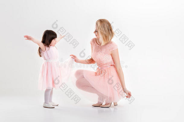 金发妈妈和可爱的小女儿穿着粉红色的裙子公主