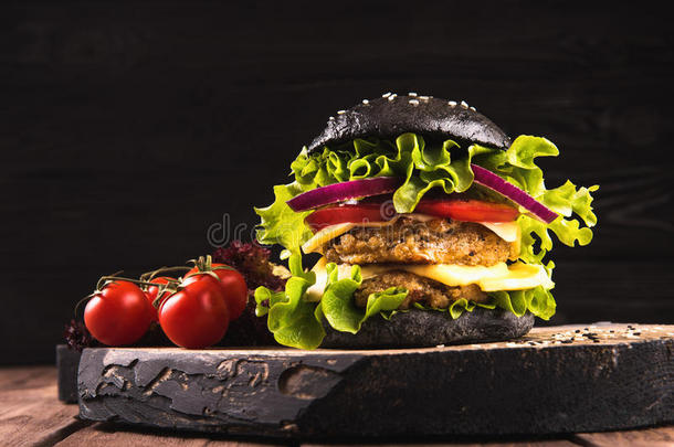 美味的自制纯素黑汉堡，两个鹰嘴豆切片，西红柿，奶酪，洋葱和沙拉在木桌上，黑暗