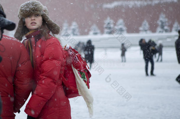 穿着红色夹克的女孩在大雪中走在红色的广场上
