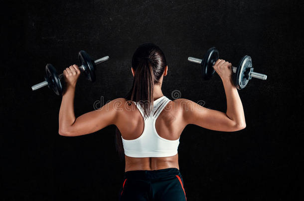 运动的年轻女人在黑色背景下做健身锻炼。 有吸引力的健身女孩用哑铃拉起肌肉。