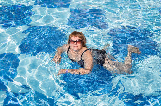 活跃的老年妇女在蓝色游泳池水中游泳