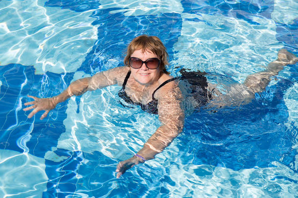 活跃的老年妇女在蓝色游泳池水中游泳