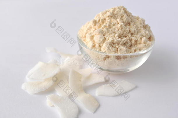 白色背景上的椰子粉和薄片。 奶油粉放在玻璃碗里。 在白色上隔离。 替代无麸质面粉