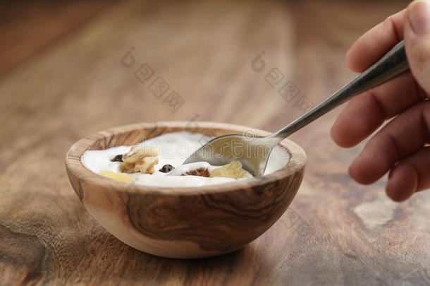 用勺子吃自制酸奶，在木桌上的木碗里放着穆斯利
