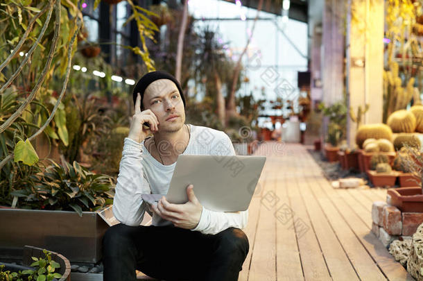 迷人的时髦男人在现代笔记本电脑上工作。 坐在阳光明媚的绿色公园里。 商业生活方式的概念