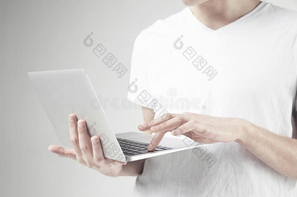 近景的现代笔记本<strong>电脑</strong>在男人的手`，男人穿<strong>白色</strong>T恤，在便携式<strong>电脑</strong>上工作。 工作室的<strong>白色</strong>背景