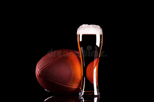 啤酒玻璃与深色啤酒泡沫和美国足球在黑色背景