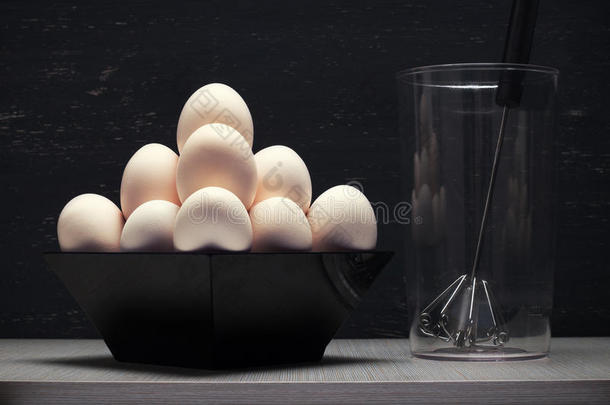 木制桌子上有鸡蛋和手搅拌机的杯子