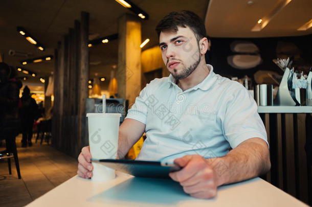 一个年轻人拿着平板电脑和一杯<strong>清爽</strong>的饮料坐在舒适的餐厅里