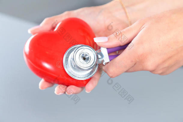 女医生手里拿着红色玩具心脏和听诊器。 心脏治疗师，心律失常的概念