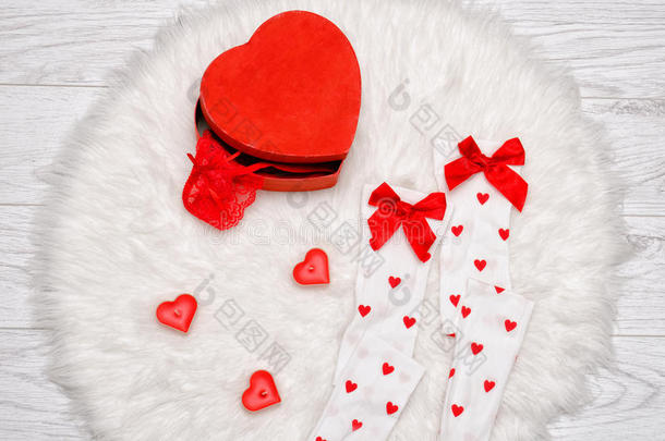 时尚概念。 红色盒子心形花边内衣，白色长袜带蝴蝶结，心形蜡烛在白色毛皮上
